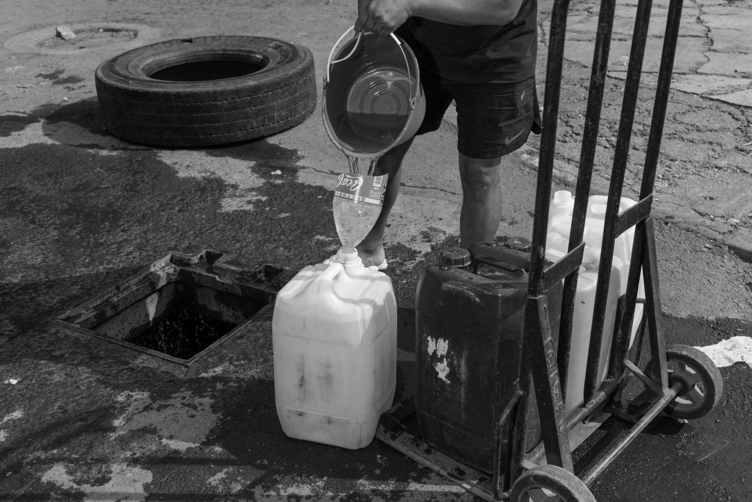 A man funnels water from the street into a jug, May 27, 2024.