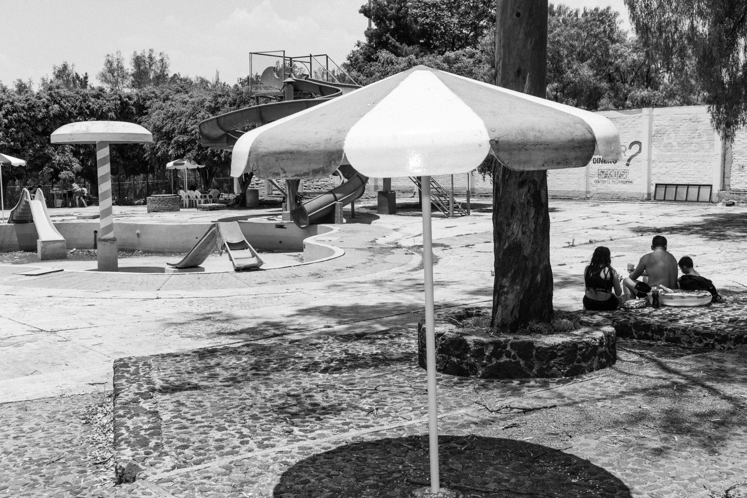 A family sits in the shade to avoid the heat near an empty pool at the Balneario Elba water park, May 26, 2024.
